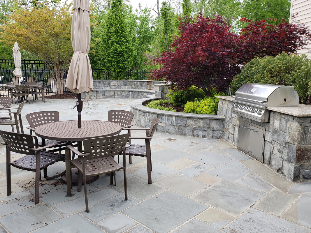A concrete patio with chairs and barbeque in a backyard